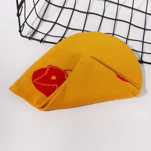 Detailed close-up of yellow knit beanie featuring red abstract jacquard pattern on white background