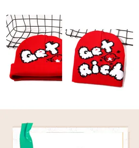 Dettaglio del berretto rosso in maglia con scritta Get Rich bianca e motivo pianeta
