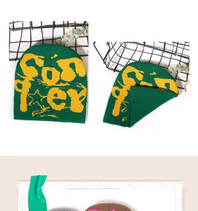 Close-up of green knit beanie with yellow graffiti jacquard lettering and star pattern