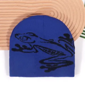 Dark blue knitted beanie with black frog pattern on a textured wooden tray background