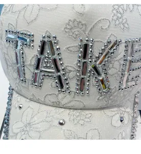 Detailed close-up of sparkling rhinestone TAKE lettering on lace floral baseball cap