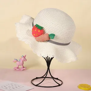 Detail of a creamy white kids straw sun hat with cute strawberry and carrot ornaments