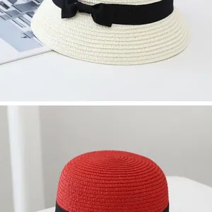 Detail view of woven straw sun hats in beige and red with black ribbon bow decoration