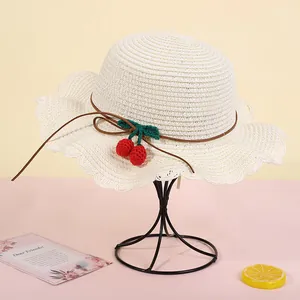 Close-up of children's cream straw hat with ruffled brim and handmade crochet cherries