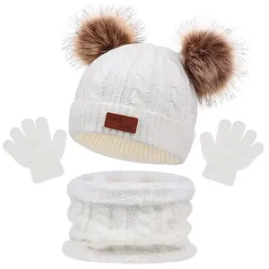 Detail of cream cable knit texture and fluffy faux fur pom-poms on kids winter set