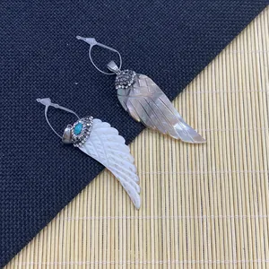 Shell wing pendants with crystal accents on a textured bamboo and blue fabric backdrop