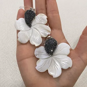 Détail de pendentifs fleurs en nacre avec cristaux tenus en main pour la taille