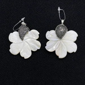Détail de pendentifs fleurs en nacre avec pavé de cristaux scintillants sur fond noir