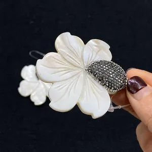 Détail de boucles d'oreilles fleur avec pétales en nacre et centre pavé de cristaux noirs