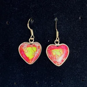 Macro detail of heart-shaped drop earrings with colorful marble stone and gold plating