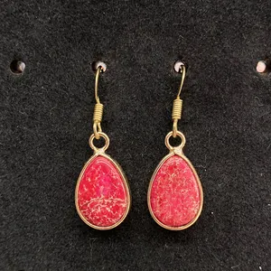 Close-up of teardrop rose red emperor stone earrings with gold metal frame on black