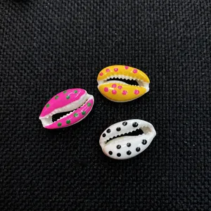 Three colorful spotted cowrie shell charms for DIY jewelry making on a black fabric background