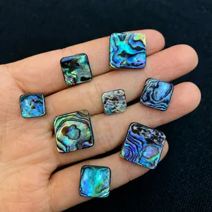 Macro shot of square abalone shell cabochons with rainbow luster in a hand for scale