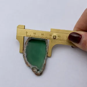 Macro detail of irregular green agate slice pendant measured with a brass caliper