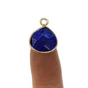 Facettierter Lapislazuli Tropfenanhänger mit Goldrand auf einer Fingerspitze