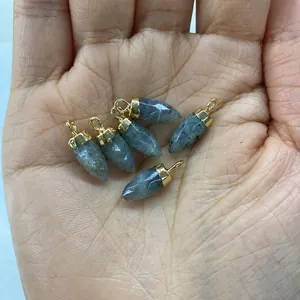 Detail of bullet-shaped labradorite pendants with gold caps held in hand for scale