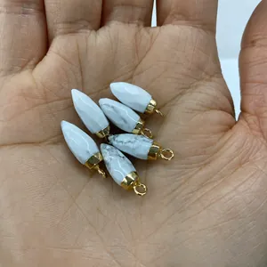Handheld view of bullet-shaped white turquoise pendant with gold metal clasp detail
