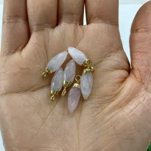 Detailed view of six bullet-shaped pink quartz stone pendants with gold metal caps held in hand
