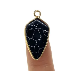 Arrowhead pendant with black stone and gold-plated frame shown on fingertips for scale