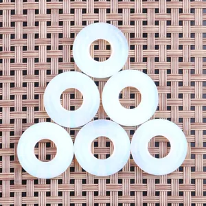 Nahaufnahme von sechs weißen Edelsteinanhängern in Donut-Form auf gewebter Matte