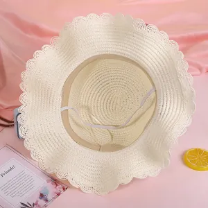 Dettaglio cappello di paglia beige con bordo in pizzo ondulato e cinturino antivento