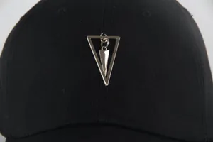 Close-up of black baseball cap featuring a unique silver metallic geometric triangle pendant