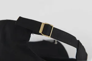 Detail of black cotton baseball cap showing adjustable bronze metal buckle and fabric strap