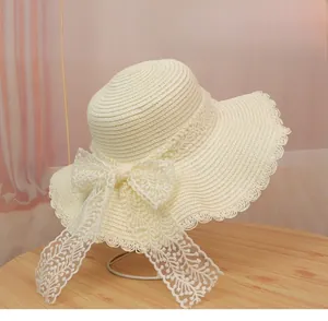 Detail of cream straw hat featuring wavy brim and elegant lace bow on a metal stand