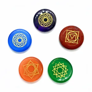 Close-up of five polished chakra stones with gold engraved symbols on a white background