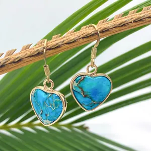 Blue heart-shaped turquoise stone drop earrings with gold rim on natural wood branch