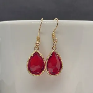 Detailed close-up of faceted red teardrop crystal earring with golden filigree edge