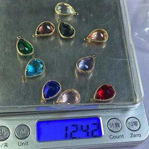 Faceted teardrop crystal pendants with gold edges displayed on a digital weighing scale