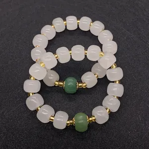 Dettaglio macro di perle a botte in giada bianca con distanziali dorati e accento verde