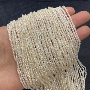 Hand holding strands of 2-3mm natural white freshwater rice pearls for DIY jewelry making