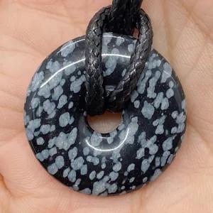 Macro shot of snowflake obsidian donut pendant with black braided cord held in palm