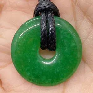 Detailed close-up of a green jade donut pendant on a hand with black woven cord