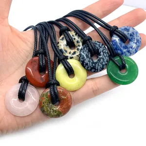 Natural tiger eye and colorful stone donut pendants held in hand for DIY necklaces