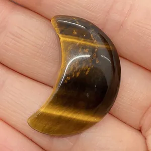 Perle en œil de tigre polie en forme de croissant dans la main montrant la texture
