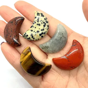 Pendentifs lune en pierres naturelles polies œil de tigre et dalmate tenus dans la main
