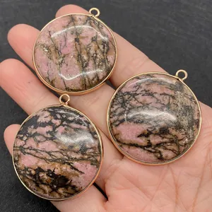 Détail macro de trois pendentifs ronds en rhodonite avec bordure dorée en main