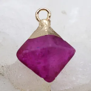 Macro detail of magenta natural stone octahedron pendant with gold metal loop