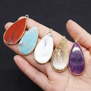 Detailed view of teardrop natural stone pendants with gold metal edges held in hand