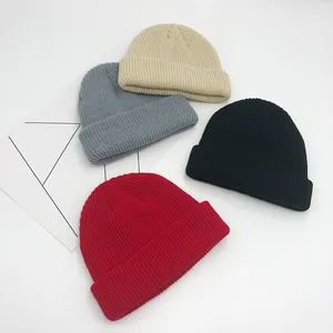 Détail du tricot côtelé des bonnets en beige, gris, noir et rouge sur fond blanc