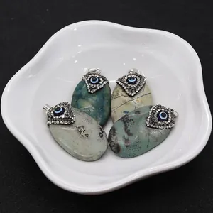 Detailed view of oval turquoise pendants with evil eye crystals on a ceramic tray
