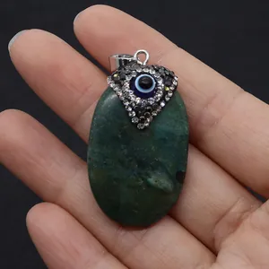 Detailed view of turquoise oval pendant with evil eye charm held by fingers
