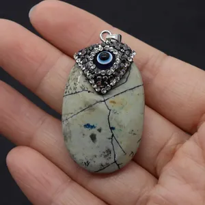 Hand holding oval turquoise pendant with evil eye design on black background