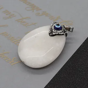 Vue détaillée du pendentif ovale en pierre blanche avec œil bleu et cristaux brillants