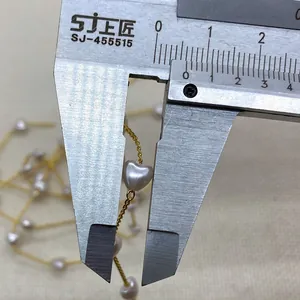Golden chain necklace with 7mm heart-shaped pearls being measured by a caliper