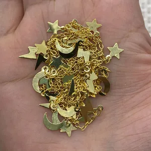 Detail of gold chain with tiny star, crescent moon, and lightning bolt charms in hand