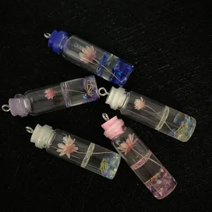 Five assorted glass cylinder pendants with dried flowers and sequins on black background